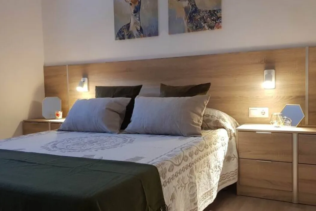     Dormitorio principal con cama de matrimonio, cabecero de madera, iluminación cálida, mesitas de noche y decoración acogedora en alojamiento turístico en Galicia