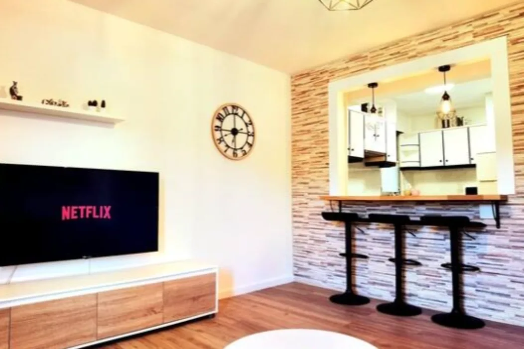 Salón moderno con televisión Smart TV, barra americana y acceso visual a la cocina en alojamiento turístico cerca de Santiago